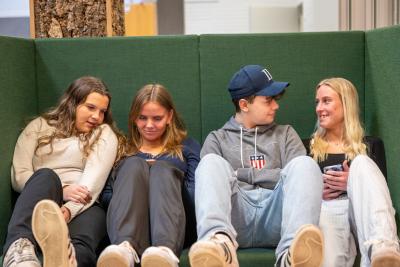 Fire skoleelever sidder i en sofa og kigger på deres mobiltelefoner