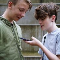 To skoleelever kigger ned på en telefon