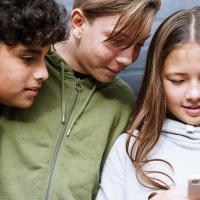 Tre skoleelever kigger ned på en mobiltelefon