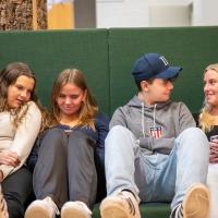 Fire skoleelever sidder i en sofa og kigger på deres mobiltelefoner